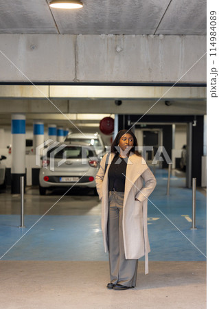 Stylish woman in elegant coat poses confidently in a parking garage, embodying casual urban fashion Stylish woman in elegant coat poses confidently in a parking garage, embodying casual urban fashion 114984089