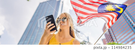 Travel and technology. Young woman tourist with the flag of Malaysia is looking at a city map in a smartphone for navigation BANNER, LONG FORMAT 114984235