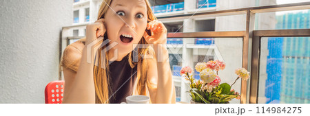 Young woman on the balcony annoyed by the building works outside. Noise concept. Air pollution from building dust BANNER, LONG FORMAT 114984275