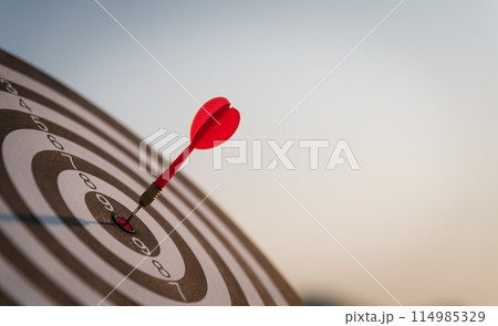 Close up shot red darts arrows in the target center on dark blue sky background. Business target or goal success and winner concept. 114985329