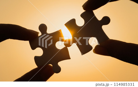 Silhouette of close up hand connecting a piece of jigsaw puzzle over sunlight effect. symbol of association,success and connection concept. business strategy. Silhouette of close up hand connecting a piece of jigsaw puzzle over sunlight effect. symbol of association,success and connection concept. business strategy. 114985331