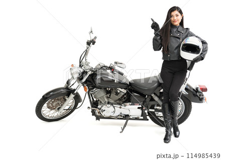 バイクの横に立って、ヘルメットを持って、指差しするバイク女子 バイクの横に立って、ヘルメットを持って、指差しするバイク女子 114985439