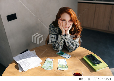 Top view of sad young unemployment woman counting remaining money sitting at home table due to economic financial crisis. Empty wallet. Bankrupt, poverty, tax, money concept. 114988404