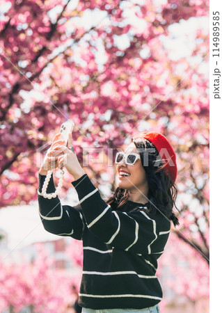 happy woman taking selfie on the phone in front of blooming sakura 114989585