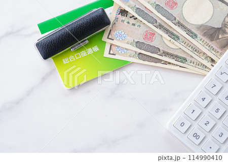 テーブルの上に置かれた銀行の預金通帳と印鑑、1万円札、電卓 114990410
