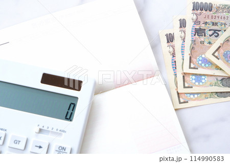 テーブルの上に開いた状態で置かれた銀行の預金通帳と、1万円札、電卓 114990583