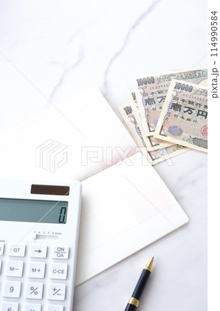 テーブルの上に開いた状態で置かれた銀行の預金通帳と、1万円札、電卓 114990584