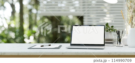A close-up image of a laptop computer white-screen mockup on a white table in a modern office room. A close-up image of a laptop computer white-screen mockup on a white table in a modern office room. 114990709