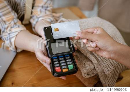 A close-up image of a customer tapping her credit card with a payment terminal in a clothing store. A close-up image of a customer tapping her credit card with a payment terminal in a clothing store. 114990908