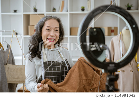 A female online seller is showing her goods live on her social media, selling clothes online. A female online seller is showing her goods live on her social media, selling clothes online. 114991042