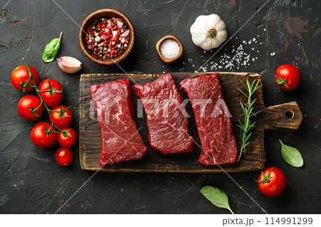 Beef raw meat, black stone background, spices, tomatoes, herbs. Top view Banner. Fresh red meat with pepper, salt for grilling on dark cutting board. Prime fillet. Food magazine style. Chief menu BBQ 114991299