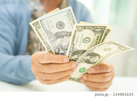 Asian senior woman holding and counting US dollar banknotes money in purse. Poverty, saving problem in retirement. Asian senior woman holding and counting US dollar banknotes money in purse. Poverty, saving problem in retirement. 114991635