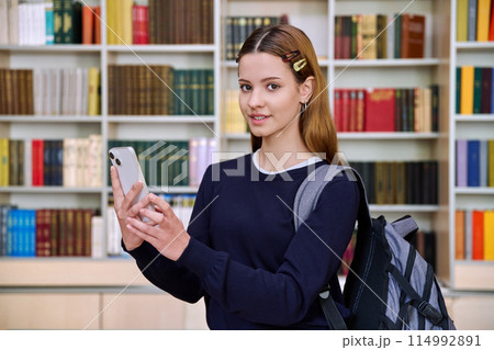 Teenage female student using smartphone, inside high school building, in library Teenage female student using smartphone, inside high school building, in library 114992891