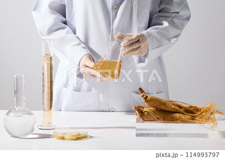 Template photo for beauty care or healthcare product has ginseng origin, a yellow liquid erlenmeyer hold by a researcher hands, a few lab glassware placed on table with vacant space in center Template photo for beauty care or healthcare product has ginseng origin, a yellow liquid erlenmeyer hold by a researcher hands, a few lab glassware placed on table with vacant space in center 114993797
