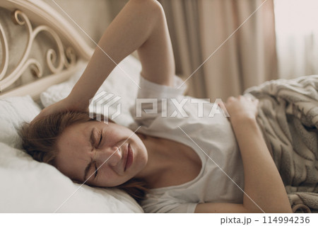 Young woman suffering with headache flu ill sick disease cold at home indoor lying on bed top view 114994236