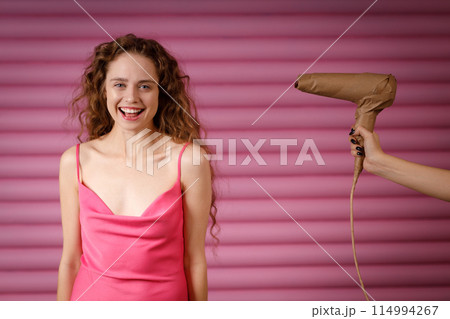 Young positive smiling woman receives surprise gift hand hold hair dryer wrapped in rustic beige craft paper. Black Friday concept on pink background. 114994267