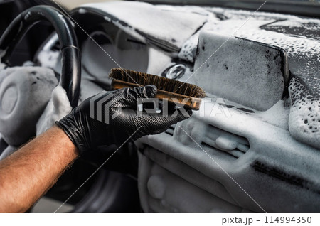 A mechanic cleans the interior of a car with a brush and foam. 114994350