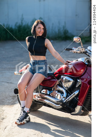 Brunette woman in shorts on a red motorcycle.  114994404