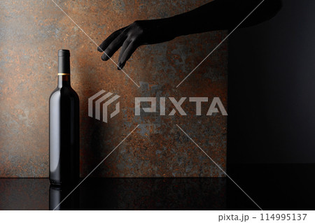 Woman hand in glove reaches for a bottle of red wine. Woman hand in glove reaches for a bottle of red wine. 114995137