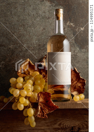 Bottle of white wine with grapes and dried up vine leaves. 114995171