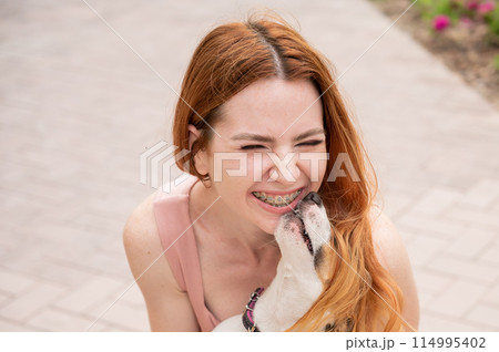 Dog jack russell terrier licks the owner in the face outdoors. Girl with braces on her teeth. Dog jack russell terrier licks the owner in the face outdoors. Girl with braces on her teeth. 114995402