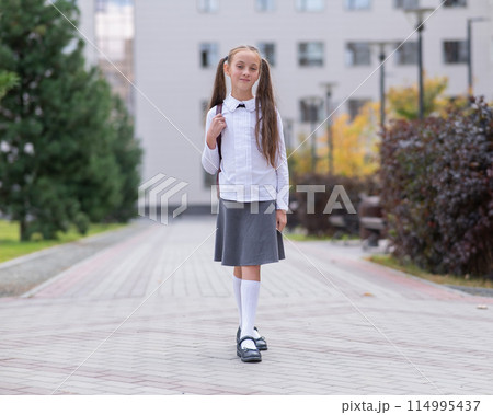 Caucasian girl in uniform and with a backpack goes from school.  114995437