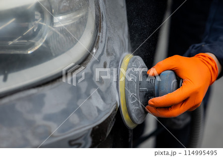 A mechanic sands the putty on a car body with a machine. Repair after an accident.  114995495