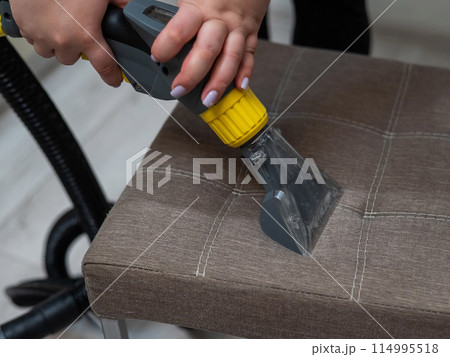 Woman cleaning a fabric chair with a professional washing vacuum cleaner. Woman cleaning a fabric chair with a professional washing vacuum cleaner. 114995518