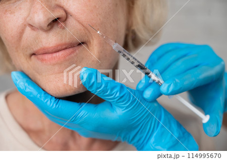 Doctor makes beauty injections in the face of an old caucasian woman. Cropped portrait.  114995670