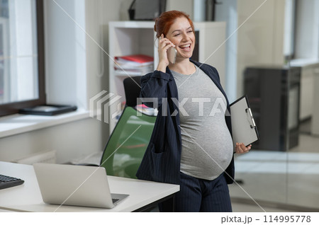 Pregnant woman using mobile phone and holding paper tablet in office.  114995778