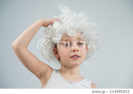 Portrait of a little Caucasian girl wearing a white curly wig on a white background.  114995852