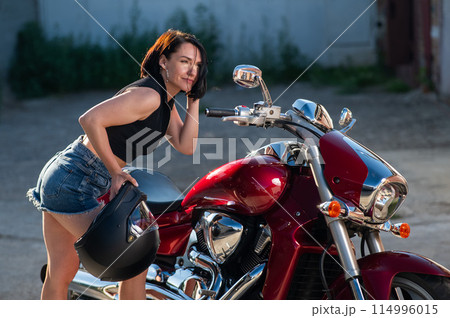 Brunette woman looks in the rearview mirror on a motorcycle. 114996015
