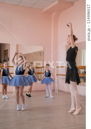 Children's ballet school. Caucasian woman teaching ballet to little girls. Vertical photo.  114996017