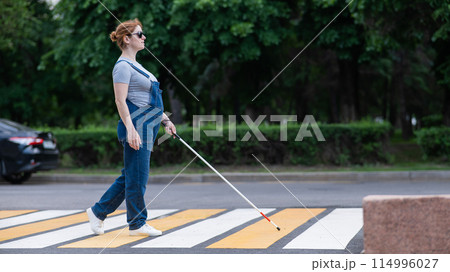 Blind pregnant woman crosses the road at a crosswalk with a cane. Blind pregnant woman crosses the road at a crosswalk with a cane. 114996027