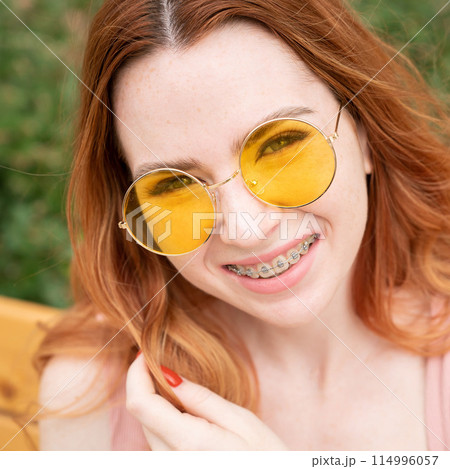 Beautiful young woman in yellow sunglasses smiling showing off braces on her teeth. Beautiful young woman in yellow sunglasses smiling showing off braces on her teeth. 114996057