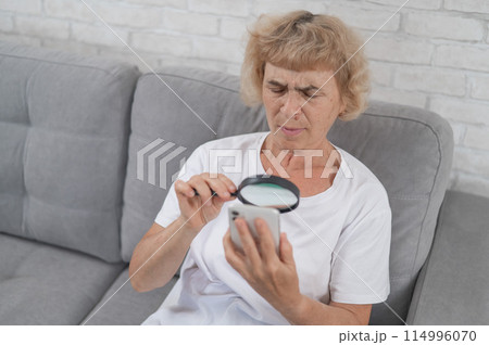 Elderly Caucasian woman with myopia and trying to read a message on a smartphone using a magnifying glass. Elderly Caucasian woman with myopia and trying to read a message on a smartphone using a magnifying glass. 114996070