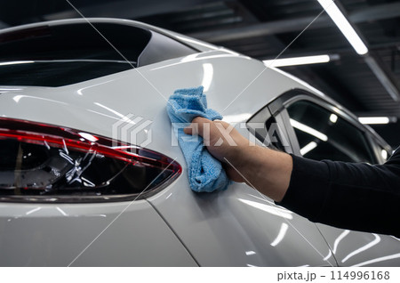 A mechanic wipes the body of a white car with a microfiber cloth.  114996168