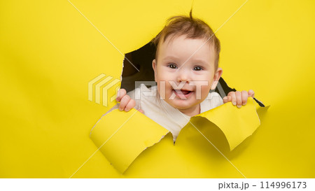 Cute Caucasian baby sticking out of a hole in a paper yellow background. Cute Caucasian baby sticking out of a hole in a paper yellow background. 114996173