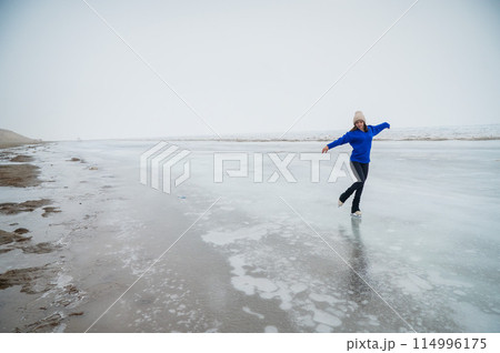 Caucasian woman in a blue sweater is skating on a frozen lake. The figure skater performs the program. 114996175