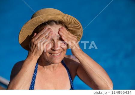 Portrait of an older woman applying sunscreen to her face while on vacation.  114996434