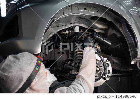 An auto mechanic applies anti-corrosion mastic to the underbody of a car. An auto mechanic applies anti-corrosion mastic to the underbody of a car. 114996646