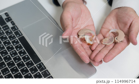 Close-up of male hands with hearing aids near laptop.  114996714