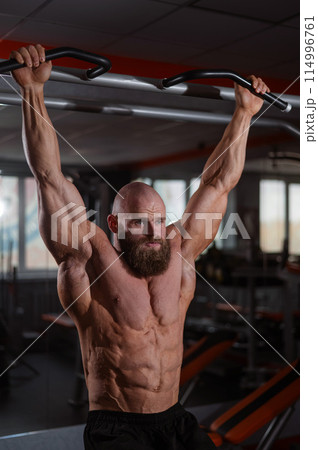 A Caucasian man hangs on a horizontal bar and raises his legs. Vertical photo. A Caucasian man hangs on a horizontal bar and raises his legs. Vertical photo. 114996761