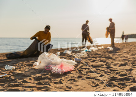 Earth day. Volunteers activists collects garbage cleaning of beach coastal zone. Woman mans with trash in garbage bag on ocean shore. Environmental conservation coastal zone cleaning. Blurred image 114996894