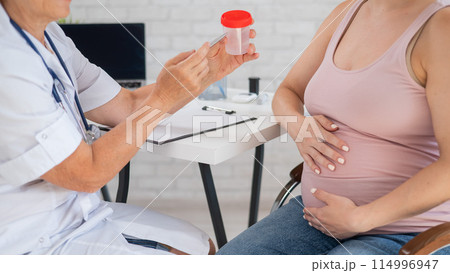 The doctor explains to a pregnant patient how to pass a urine test. The doctor explains to a pregnant patient how to pass a urine test. 114996947