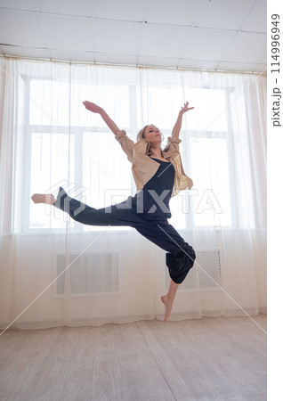 Caucasian woman dances contemporary in ballet class. Dancer in a jump. Vertical photo. 114996949