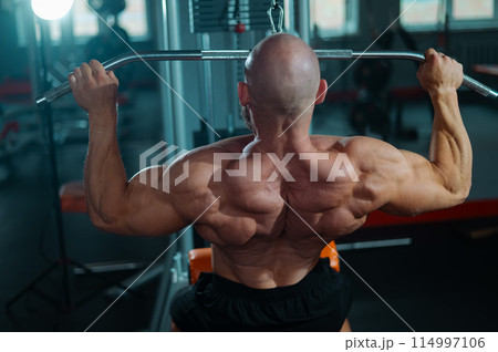 Caucasian man doing lat pull-downs on a machine. Caucasian man doing lat pull-downs on a machine. 114997106