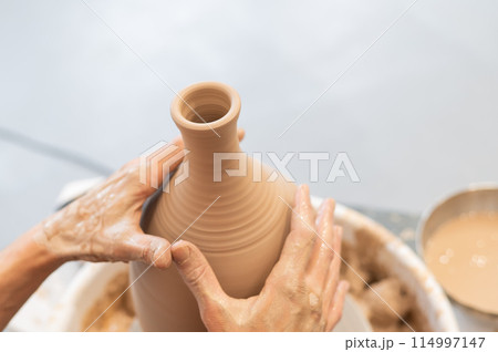 Close-up of a potter's hands making a ceramic vase on a potter's wheel. 114997147