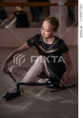 Woman sitting on the floor and tying ribbons on her pointe shoes. Vertical photo. Woman sitting on the floor and tying ribbons on her pointe shoes. Vertical photo. 114997163