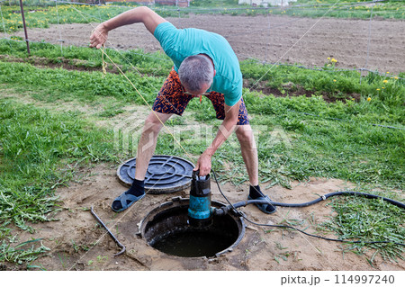 When servicing a septic tank, a man uses a submersible wastewater pump. 114997240